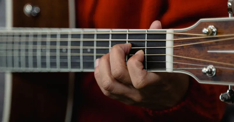Detailed view of a hand playing a chord on an acoustic guitar, showcasing the fretboard and strings.