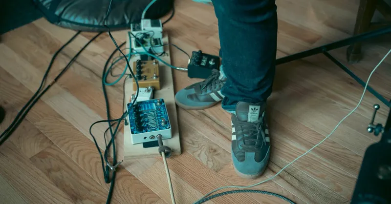 Casual musician setting with foot on a set of guitar effects pedals on a wooden floor.