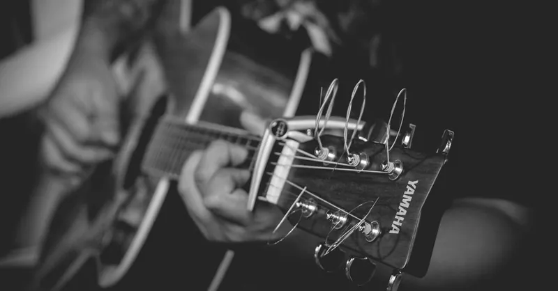 Black and white close-up of acoustic guitar being played, emphasizing strings and details.
