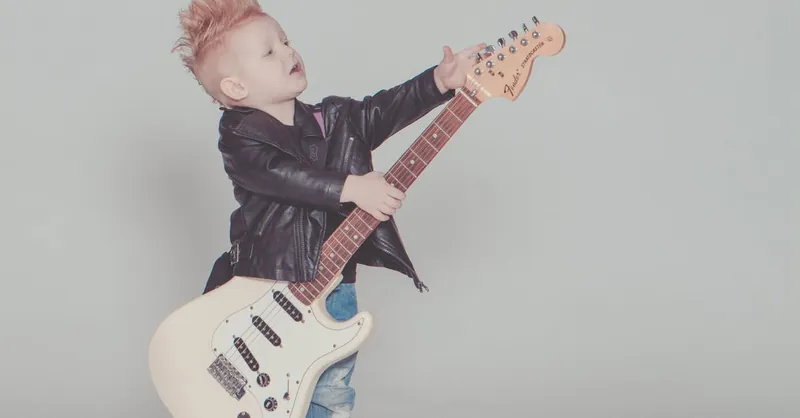 Stylish young boy with a mohawk strumming an electric guitar, wearing a leather jacket and blue jeans.
