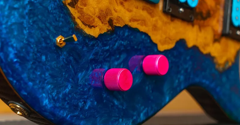 Close-up of a colorful electric guitar with pink and blue knobs, highlighting its vibrant design.