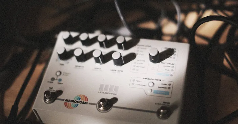 Close-up of audio effects pedal surrounded by cables in a dimly lit music studio, showcasing music technology.