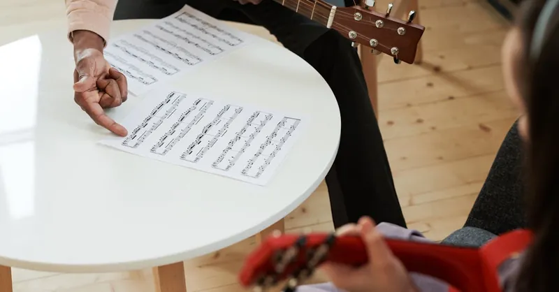 Hands demonstrating music on an acoustic guitar with sheet music, ideal for learning concepts.