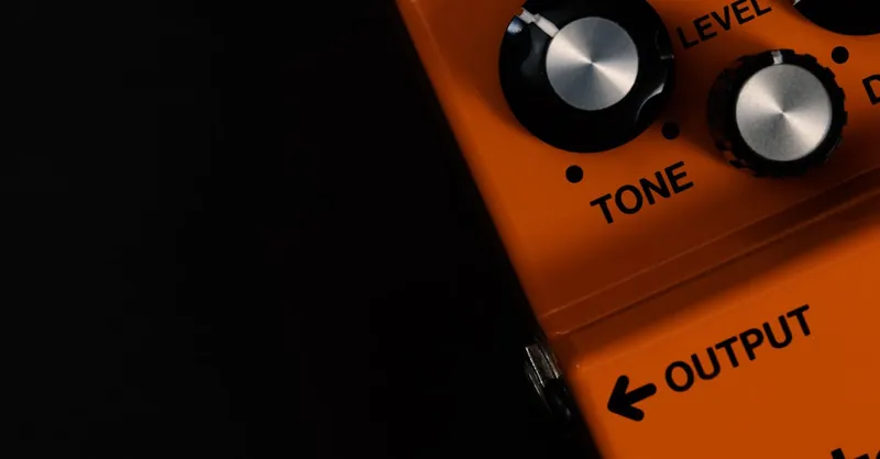Detailed close-up of an orange guitar distortion pedal showcasing tone and level knobs.