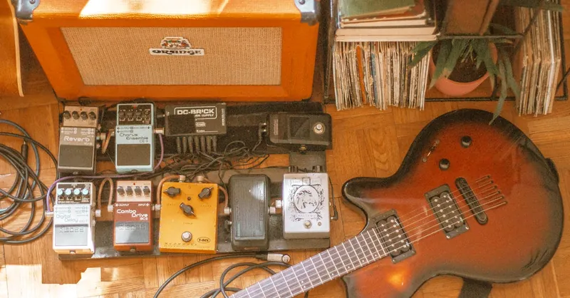 Vintage electric guitar and amplifier setup with various effects pedals on a wooden floor.