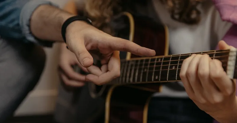 A detailed view of hands during a guitar lesson, focusing on finger placement and technique.
