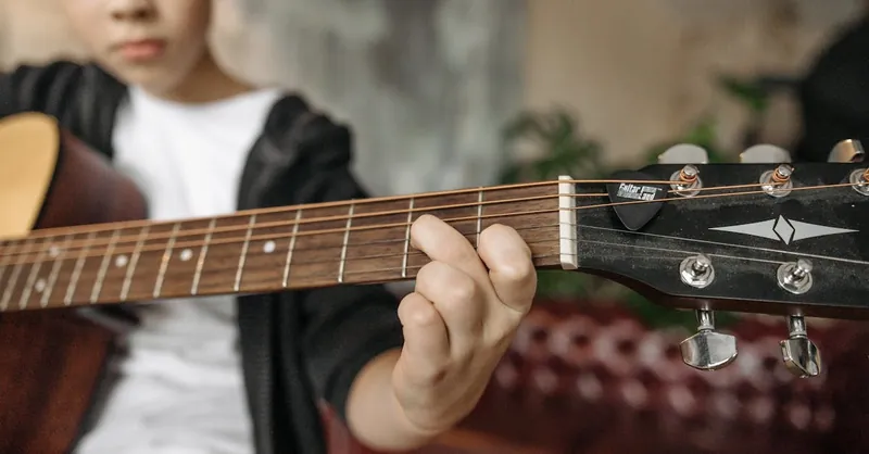A child playing an acoustic guitar indoors with focus on fretboard and fingers.