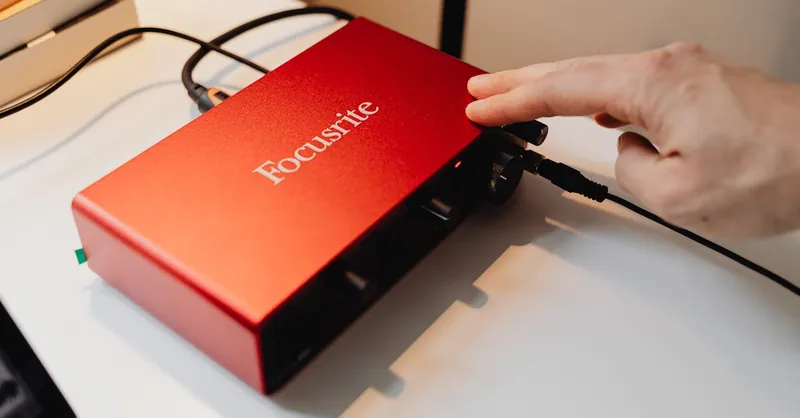 Detailed view of a red audio interface being operated by a hand on a desk.