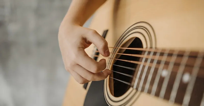 Detailed view of a hand strumming an acoustic guitar, showcasing the strings and soundhole.