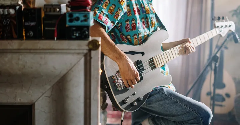 Musician playing electric guitar in a cozy home music studio with audio equipment.