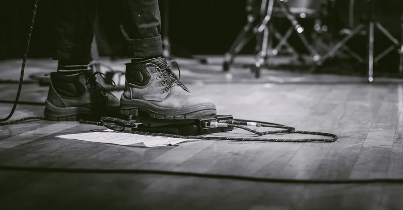 Black and white image of a performer using guitar pedal at a live concert.