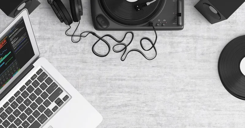 Flat lay of a music workspace with a laptop, headphones, turntable, and speakers on a desk.