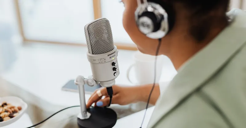 Woman using a microphone and headphones indoors, focusing on recording a podcast or voiceover.
