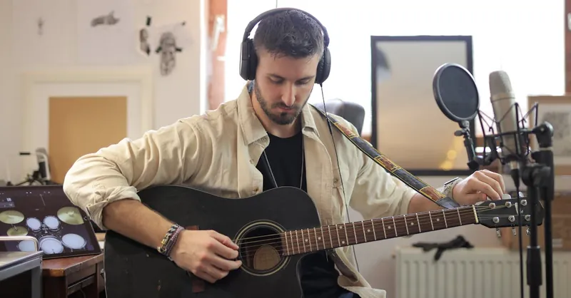 Musician adjusting guitar strings in modern recording studio environment.