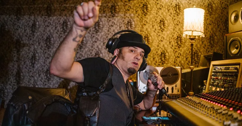 Music producer working with mixing console and microphone in a recording studio.