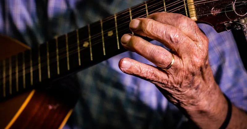 Close-up of an elderly hand playing guitar, showcasing texture and focus on strings