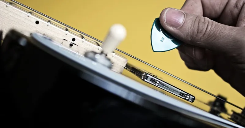 Detailed view of hand using a green guitar pick on an electric guitar with yellow background.