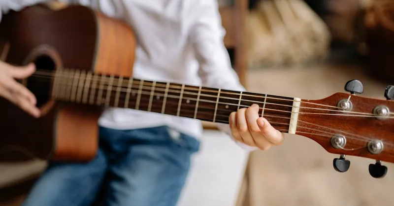 A close-up of a child practicing guitar chords indoors, emphasizing hands and strings.
